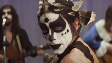 Cena do filme Homem com H (2025), com Jesuíta Barbosa caracterizado como Ney Matogrosso, usando maquiagem artística em preto e branco e penas na cabeça, recriando a estética teatral e performática dos shows do cantor brasileiro nos anos 1970