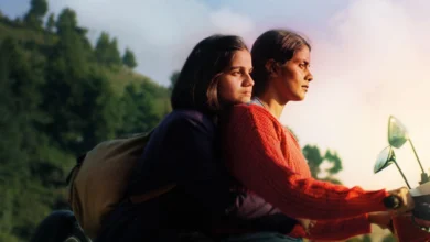 Cena do filme Sempre Garotas (2024), com Preeti Panigrahi e Kani Kusruti em uma moto, percorrendo uma estrada cercada pela natureza.