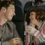 Cena do filme Os Roses: Até Que a Morte Os Separe (2025), com Benedict Cumberbatch e Olivia Colman trocando olhares apaixonados durante um voo.