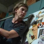 Austin Butler segura um taco de beisebol com expressão tensa em cena do filme Ladrões (2025), ao lado de uma geladeira cheia de imãs e bilhetes.