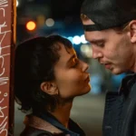 Austin Butler e Zoë Kravitz em uma cena romântica noturna do filme Ladrões (2025), dirigindo olhares intensos um para o outro próximos a uma parede com grafites.