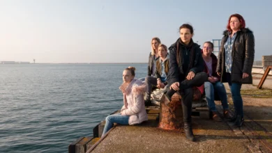 Cena do filme Entre Dois Mundos (2021), com Juliette Binoche e outras personagens sentadas em um cais à beira-mar.