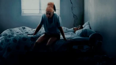 Cena do filme Até a Última Gota (2025), da Netflix, mostrando a personagem vivida por Taraji P. Henson sentada na beira da cama em um quarto escuro e desgastado, com uma criança dormindo ao fundo. Drama dirigido por Tyler Perry com estreia em 6 de junho de 2025.