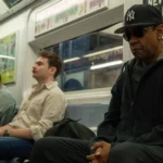 Cena do filme "Highest 2 Lowest" (2025), dirigido por Spike Lee, com Denzel Washington sentado em um metrô de Nova York, usando boné dos Yankees e óculos escuros, em clima tenso e introspectivo.