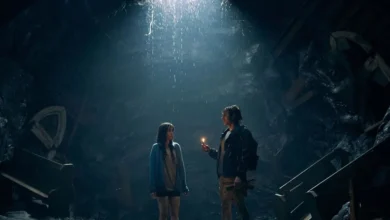 Cena do filme Juntos (2025), terror dirigido por Michael Shanks, com os atores Dave Franco e Alison Brie em uma caverna escura, sob um feixe de luz e rodeados por destroços, em clima de tensão.