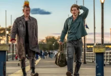 Cena do filme Ladrões (2025), com Matt Smith de moicano e casaco punk ao lado de Austin Butler, que carrega uma mochila em uma passarela ao entardecer.