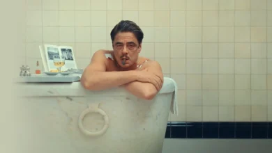 Benicio Del Toro relaxa em uma banheira, fumando um charuto, em uma cena do filme O Esquema Fenício (2025).