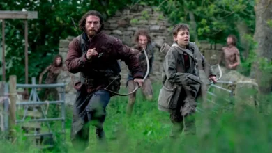 Cena do filme Extermínio: A Evolução (28 Years Later) mostrando Aaron Taylor-Johnson e Alfie Williams correndo armados com arcos em um campo verdejante, perseguidos por figuras ameaçadoras ao fundo.