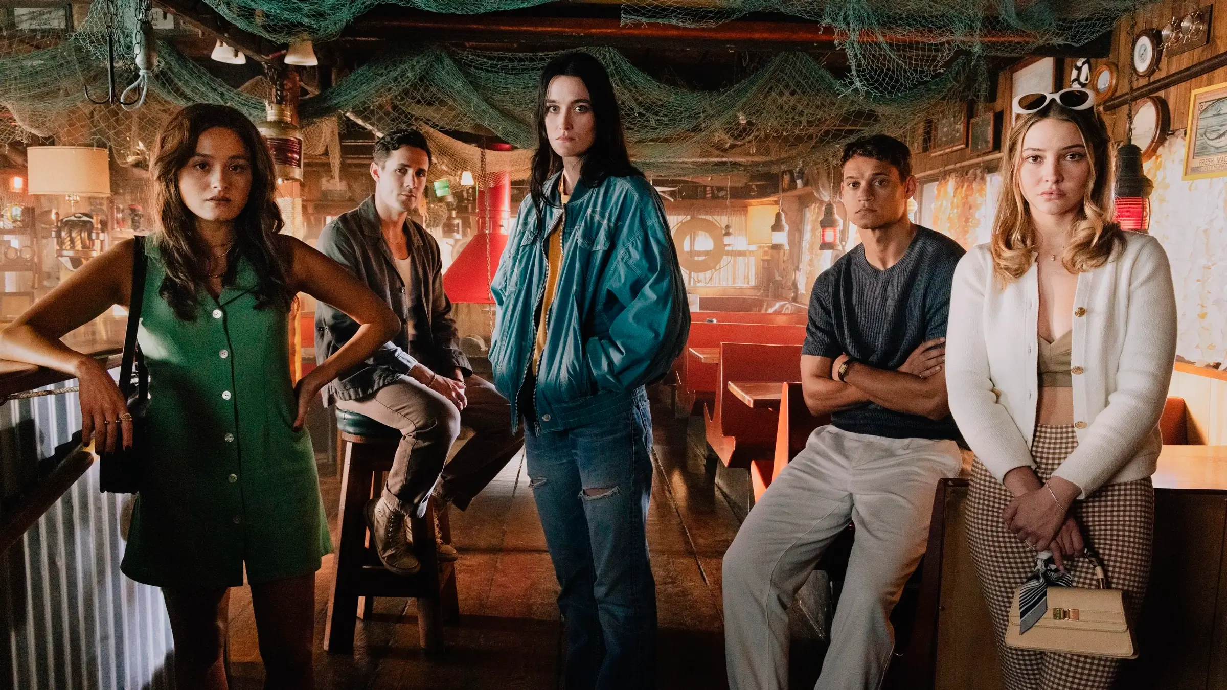 Elenco de Eu Sei o que Vocês Fizeram no Verão Passado (2025) com Tyriq Withers, Madelyn Cline, Chase Sui Wonders, Jonah Hauer-King e Sarah Pidgeon posando em um bar rústico com iluminação baixa; todos com expressões sérias, refletindo o clima de suspense do filme.
