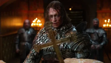 Cena do filme Drácula: Uma História de Amor Eterno, com Caleb Landry Jones usando armadura medieval e segurando uma cruz dourada.