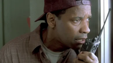 Denzel Washington como John Quincy Archibald falando no walkie talkie em cena do filme Um Ato de Coragem, usando boné vermelho e camisa xadrez