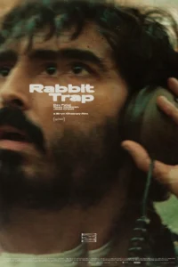 Pôster do filme de terror A Armadilha do Coelho (Rabbit Trap), com Dev Patel ouvindo fones de ouvido em close-up, destaque para atmosfera tensa e misteriosa.