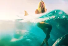 Hassie Harrison em cena de Animais Perigosos (2025), cercada por tubarões no mar no filme de terror estrelado por Jai Courtney.
