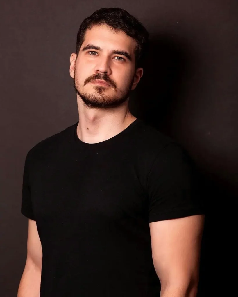 Ator Pedro Colombelli posando para foto em estúdio, usando camiseta preta, em retrato profissional.