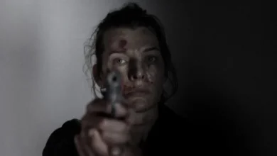 Milla Jovovich ferida apontando uma arma em cena tensa do filme Vingadora (2025), dirigido por Adrian Grunberg