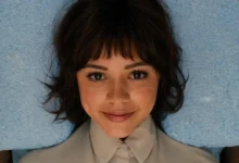 Jenna Ortega como Klara em cena do filme de ficção científica Klara e o Sol (2026), dirigida por Taika Waititi, deitada em uma superfície azul e olhando diretamente para a câmera.