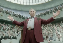 Tom Cruise em cena do Trailer de Digger, filme dirigido por Alejandro G. Iñárritu, durante um discurso em um grande tribunal cercado por uma multidão de espectadores.