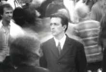 Jeremy Theobald como Bill parado entre uma multidão em cena do filme Following (Seguinte) (1998), dirigido por Christopher Nolan.