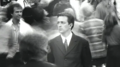 Jeremy Theobald como Bill parado entre uma multidão em cena do filme Following (Seguinte) (1998), dirigido por Christopher Nolan.