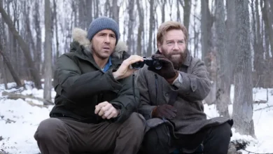Kenneth Branagh e Ryan Reynolds observam a distância com binóculos em uma floresta coberta de neve em uma cena de Mayday (2026).