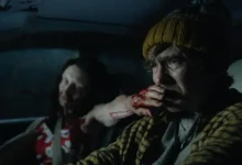 Austin Abrams dirige um carro à noite com uma mulher infectada ao seu lado em cena de Resident Evil (2026)