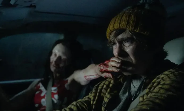 Austin Abrams dirige um carro à noite com uma mulher infectada ao seu lado em cena de Resident Evil (2026)