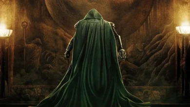 Robert Downey Jr. como Victor von Doom (Doctor Doom) diante de um enorme portal em Vingadores: Doutor Destino (2026), usando sua capa verde e segurando a máscara do vilão.