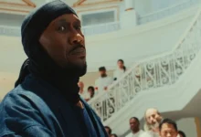 Mahershala Ali em cena de Your Mother Your Mother Your Mother (2026), em um salão com escadaria ao fundo durante momento de tensão no filme.