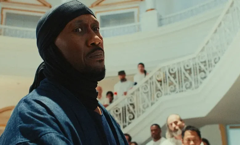 Mahershala Ali em cena de Your Mother Your Mother Your Mother (2026), em um salão com escadaria ao fundo durante momento de tensão no filme.