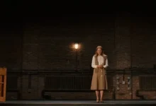 Julianne Moore em cena do filme A Grande Estreia (2026), em pé sobre um palco com paredes de tijolos e iluminação intimista.