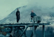 Erik Hivju e Renate Reinsve em uma cena do filme Fjord (2026), ao lado de um fiorde cercado por montanhas cobertas de neve.