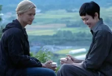 Virginie Efira e Tao Okamoto em cena do filme O Sentido da Vida (2026), sentados em uma paisagem rural, em um momento de conversa.