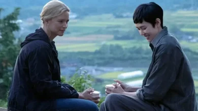 Virginie Efira e Tao Okamoto em cena do filme O Sentido da Vida (2026), sentados em uma paisagem rural, em um momento de conversa.