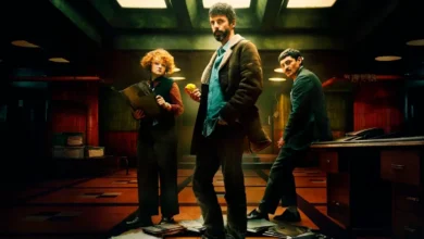 Imagem promocional da série Departamento Q da Netflix, com os atores Leah Byrne, Matthew Goode (ao centro, segurando uma bola de tênis) e Alexej Manvelov em um ambiente sombrio de escritório com iluminação dramática. Estreia em 29 de maio de 2025.