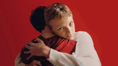 Eden Dambrine e Gustav De Waele se abraçam com força diante de um fundo vermelho vibrante em cena do filme Close (2022), de Lukas Dhont, expressando profunda conexão emocional.