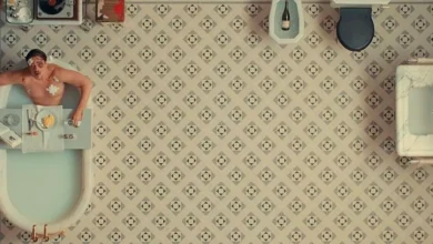 Benicio Del Toro em cena estilizada de O Esquema Fenício, dentro de uma banheira, com o cenário visto de cima em simetria geométrica.