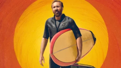 Imagem promocional do filme O Surfista com Nicolas Cage segurando uma prancha de surfe, usando roupa de neoprene, com um pôr do sol vibrante em tons de laranja e amarelo ao fundo.