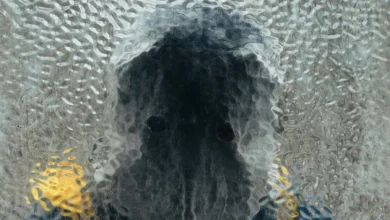 Silhueta de uma figura encapuzada atrás de um vidro texturizado em cena do filme Cloud – Nuvem de Vingança (2024)