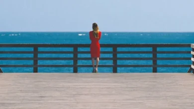 Cena do filme Réquiem para um Sonho (2000) com mulher de vestido vermelho olhando para o mar em um píer.