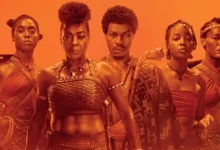 Elenco principal de A Mulher Rei (2022) com Viola Davis, Lashana Lynch, John Boyega, Sheila Atim e Thuso Mbedu em destaque sobre fundo alaranjado.