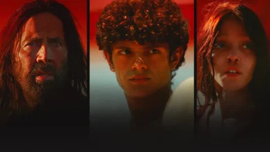 Nicolas Cage, FKA twigs e Noah Jupe em cena promocional do filme Sombras no Deserto (2025), sob luz avermelhada.