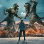 Cena épica de O Troll da Montanha 2 com dois trolls gigantes em batalha enquanto a protagonista observa a destruição na cidade ao fundo.