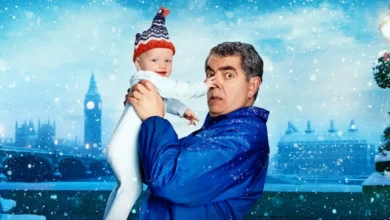 Rowan Atkinson segurando um bebê que puxa seu nariz em cena promocional da série de comédia Homem X Bebê (Man vs Baby), da Netflix.
