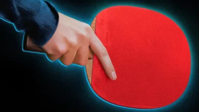 Mão segurando raquete de tênis de mesa em imagem promocional de Marty Supreme, drama dirigido por Josh Safdie e estrelado por Timothée Chalamet.