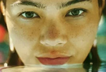 Maya da Costa em cena de Girls Like Girls (2026), em um close-up destacando sua expressão intensa e o rosto parcialmente refletido na água.