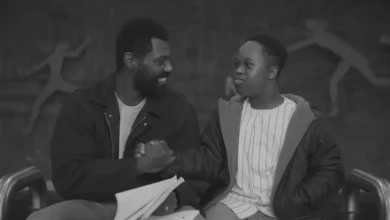 William Catlett e Jeremiah Alexander Daniels em cena de O Livro de Colorir (2024), compartilhando um momento de cumplicidade e amizade durante a jornada emocionante retratada no drama.