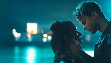 Matthew Broome e Asha Banks em uma cena romântica sob a chuva no filme Sua Culpa: Londres (2026), iluminados por luzes azuis durante um momento emocional.