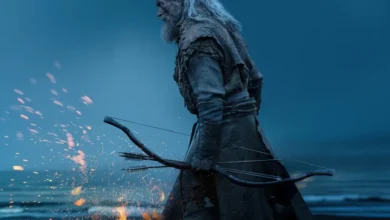 Hugh Jackman como Robin Hood em cena de A Morte de Robin Hood (2026), caminhando por uma praia sombria com arco e flechas nas mãos, cercado por faíscas e atmosfera melancólica.