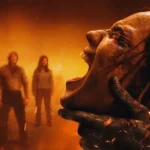 Imagem oficial de divulgação de Morte do Demônio: Em Chamas (Evil Dead Burn) mostra uma figura demoníaca segurando o próprio rosto enquanto quatro pessoas observam ao fundo em meio ao fogo.