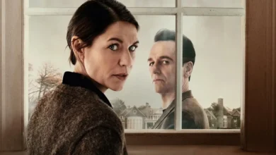 Claire Danes e Matthew Rhys em cena de O Monstro em Mim (2025), série da Netflix, diante da janela de uma casa com uma vizinhança ao fundo.